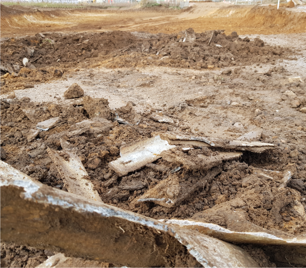 Brown soil and debris is scattered across the contaminated site, with asbestos clearly present. BSH undertook asbestos removal, to which an asbestos survey was completed first, to better understand the safety of the site.