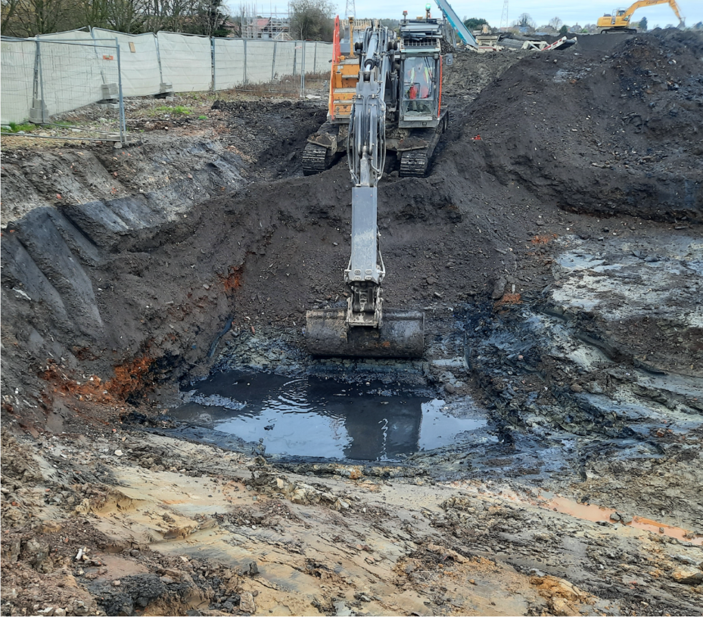 An excavator is scooping soil from this evidently contaminated site. Asbestos is present, and the earth is very uneven. This land will undergo earthworks by BSH to reshape the site’s terrain by digging deeper and moving large quantities of rock and soil.