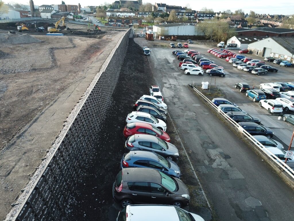 An eco crib wall situated next to a car park filled with cars, which is a temporary structure during works on this site.